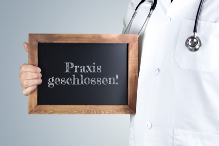 Mediziner hält ein Schild mit der Aufschrift 'Praxis geschlossen'